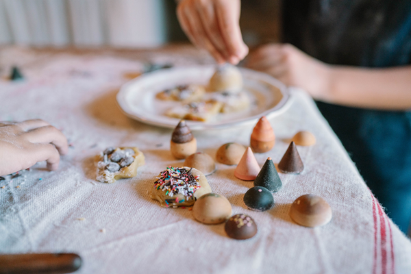Children decorate cookies with candy cones and sprinkles on a cloth-covered table, surrounded by Grapat Play Set - Bakes toys for extra fun. A plate of decorated cookies is in the background while hands get creative in the foreground.