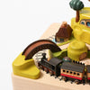 A Wooden Train Music Box - Spring set with a black locomotive and colorful accessories, including a bridge, buildings, and trees, all crafted from sustainably sourced wood, arranged on tracks on a white background.