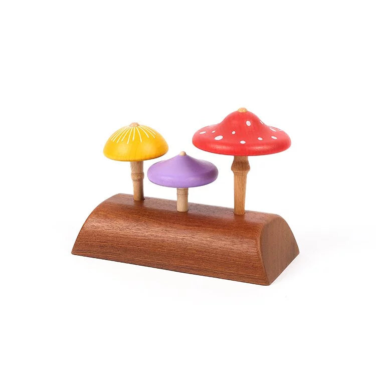 Three Wooden Mushroom Spinning Tops on a curved wooden base, with varying sizes and colors including yellow, purple, and red with white spots, crafted from responsibly-sourced wood, isolated on a white background.