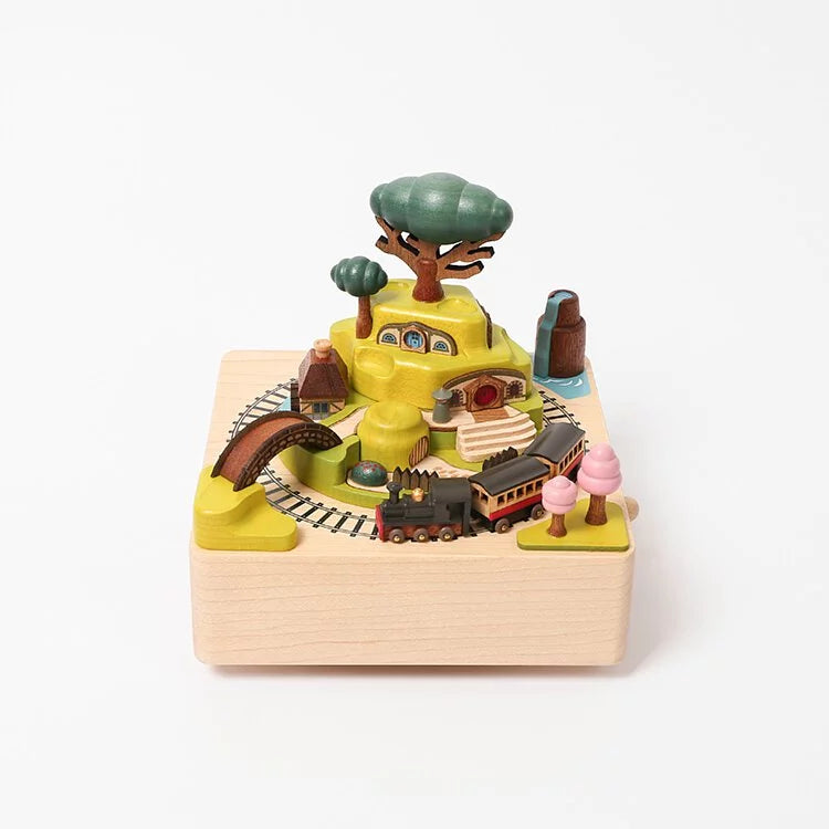 A Wooden Train Music Box - Spring scene featuring a train track winding around miniature trees, buildings, and a tunnel, all arranged on a square wooden base.