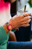 A person wearing a pink Mini Kyomo Watch - Disco and gold rings holds a glass jar with a metal spoon, dressed in a green sweater and a white and pink gradient top.