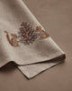 The Coral & Tusk Chipmunks with Pinecone Tea Towel features embroidered brown and tan baby animals beside a pine cone, accented with silver metallic stitching on beige linen and neatly folded on a neutral surface.