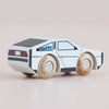 The No. 23 GT130 Dexter, a small futuristic wooden car painted white with black details and resembling a modern toy car, is displayed on a light background—perfect for imaginative play. Available for pre-order August 2026.