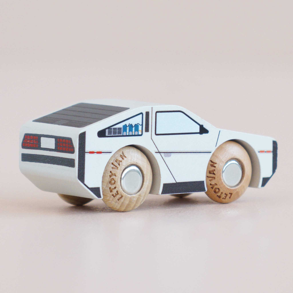 The No. 23 GT130 Dexter, a small futuristic wooden car painted white with black details and resembling a modern toy car, is displayed on a light background—perfect for imaginative play. Available for pre-order August 2026.