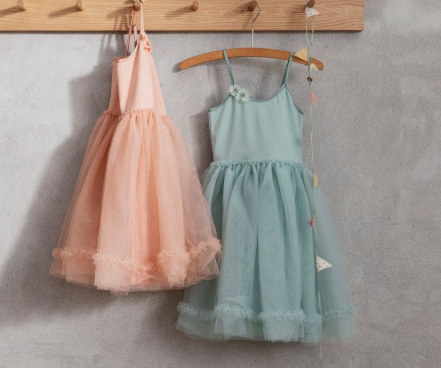 Two children's dresses on wooden hangers. The dress on the left is peach with ruffled tulle, while the one on the right is a Maileg Princess Tulle Dress - Mint with thin straps and matching ruffled tulle. Both dresses, crafted from exclusive materials, hang on a wooden rack against a light gray wall as if plucked from a Magical Wardrobe.