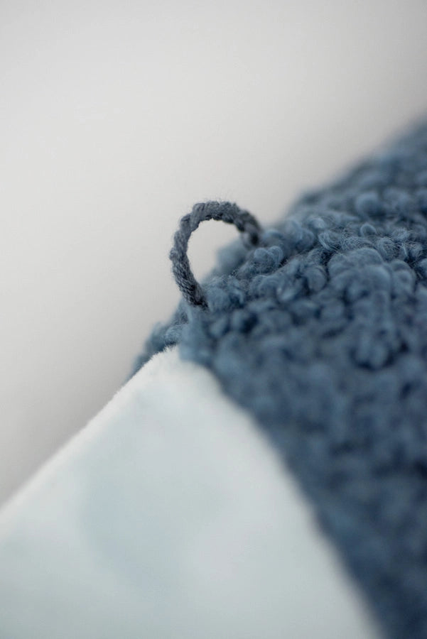 Close-up of a decorative loop on a Dark Blue Fish Pack, possibly a towel, with a soft white backing blurred in the background. Focus on the detailed texture of the loop.