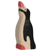 A small Holztiger Penguin figurine, featuring a raised head, handcrafted and painted in black, white, and red tones, standing upright and facing to the left.