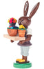 A cherished Collectible Dregeno Easter Figure - Bunny Florist balancing chocolate on one foot and serving vibrant frosted cupcakes on a tray, isolated on a white background.