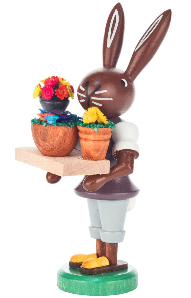 A cherished Collectible Dregeno Easter Figure - Bunny Florist balancing chocolate on one foot and serving vibrant frosted cupcakes on a tray, isolated on a white background.