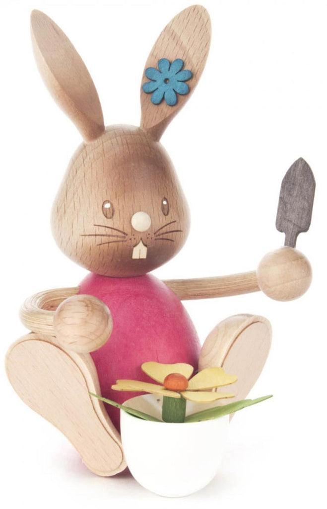 Collectible Dregeno Easter Figure - Rabbit Gardener With Flower Pot with articulated limbs, holding a small spade and a potted flower. Made in Germany, the bunny has a brown body, pink torso, and a blue flower decoration on