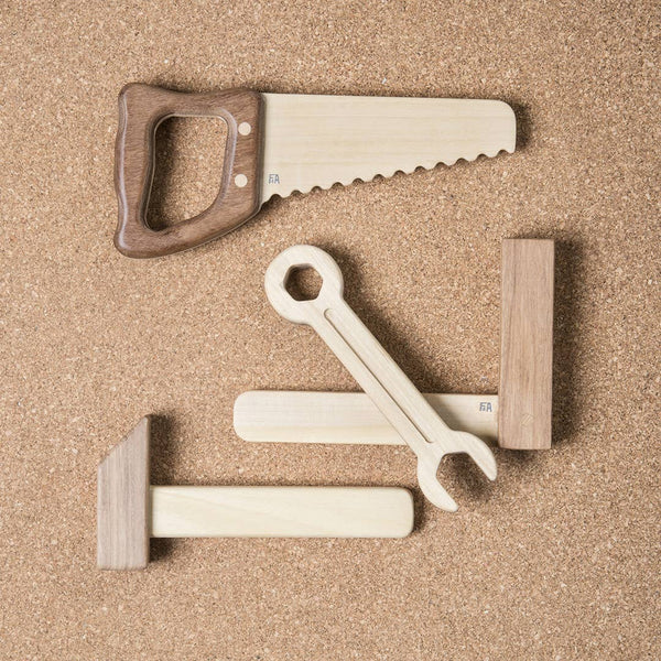 The Wooden Tool Set includes a saw, wrench, hammer, and mallet made from solid rubber wood and Sapele teak. Resting on a corkboard background, these toys showcase light and dark tones with clean, minimalist designs.