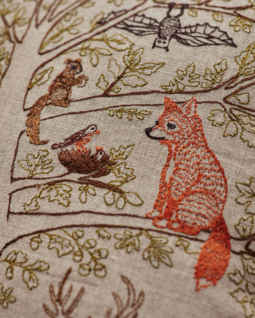 The Coral & Tusk Woodland Living Tree Pillow features embroidered woodland animals—a fox, bat, squirrel, two birds in a nest—and leafy branches. Ships in one week.