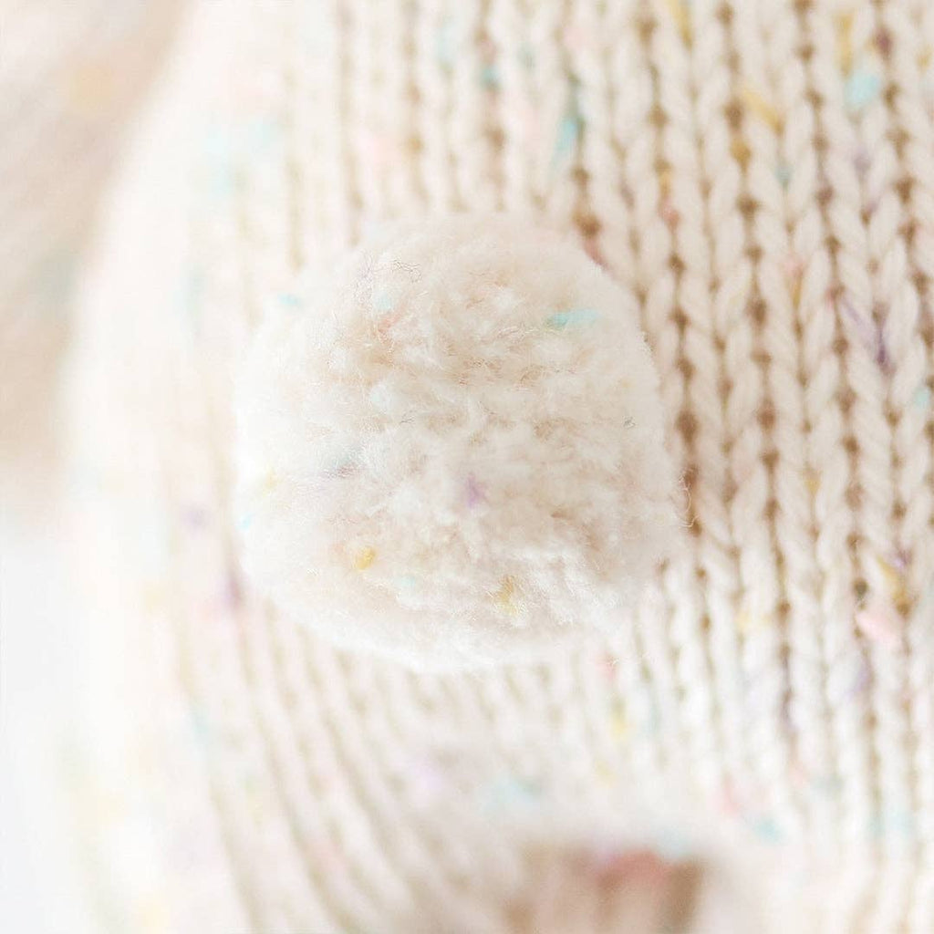 Close-up of the Cuddle + Kind Baby Bunny - Confetti shows a soft, white yarn pom-pom and hand-knit cozy texture with pastel speckles, highlighting its gentle and cuddly appearance.