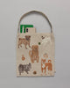 The Dogs and Toys Tote is a playful bag with embroidered dogs in various poses and designs. It holds a green notebook, a pen, and a smartphone. The background color of the tote is solid gray.