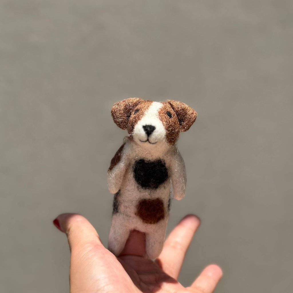 A hand holds the "Felt Finger Puppet: Jack Russell Terrier Dog," a small wool felt puppet with brown, black, and white patches, against a plain light gray background.