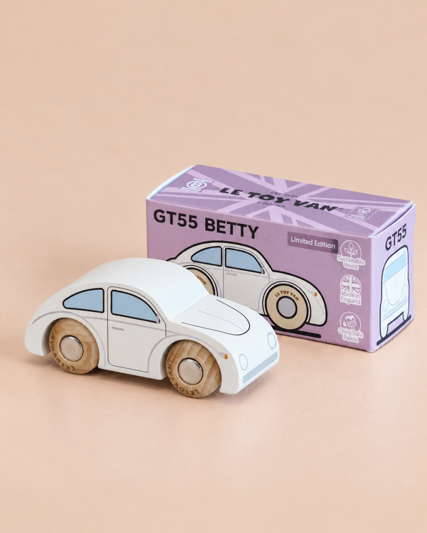 A small white classic wooden toy car with beige wheels, the No. 9 GT55 Betty | Made in England, sits beside its purple box labeled “GT55 BETTY” and “Limited Edition” on a light beige surface, evoking the nostalgic charm of a timeless toy perfect for imaginative play.