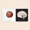 In Baby's Tummy Time Sports, an open, high-contrast board book displays a drawing of a basketball on the left page and a basketball hoop with a net on the right page. Each illustration is labeled with the words "Basketball" and "Basketball Hoop," offering visual stimulation that’s ideal for tummy time.