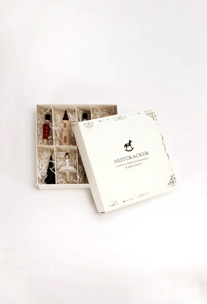 A white Sabo Concept Christmas Ornaments gift box with a rocking horse lid design, partially open to show six hand-painted wooden ornaments nestled in shredded white paper.