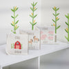 The Little Farm Soft Book set includes three embroidered books—“One Barn,” “Three Horses,” and “Five Pigs”—making a perfect farm-themed gift for infants. Displayed on a white shelf with plant decals in the background.