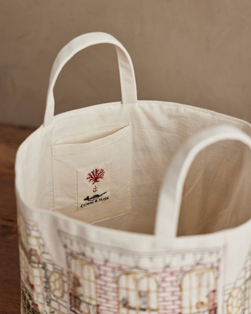 A close-up of the Home for the Holidays Bucket shows two handles, an interior pocket, and a sewn label with a red coral and "CORAL & TUSK." The bag’s building pattern makes it ideal for embroidered storage or festive Christmas decor.