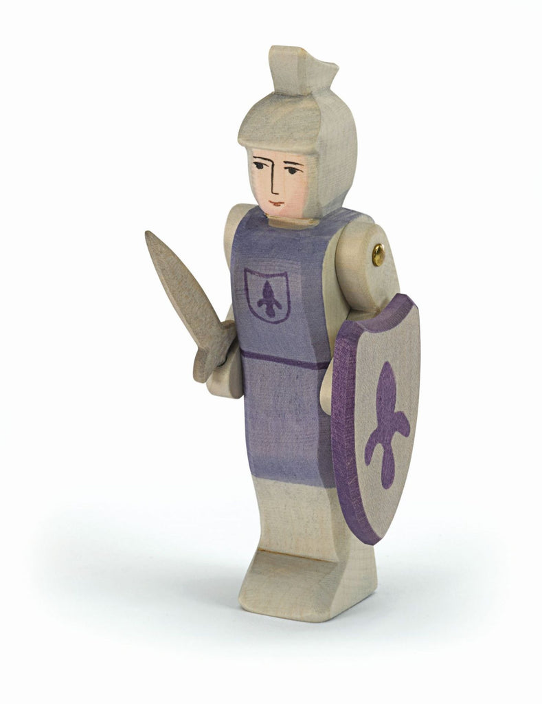 The Ostheimer Blue Knight - Standing is a handcrafted wooden toy knight with light hair, dressed in blue armor, holding a sword and shield—perfect for imaginative play on any white background.