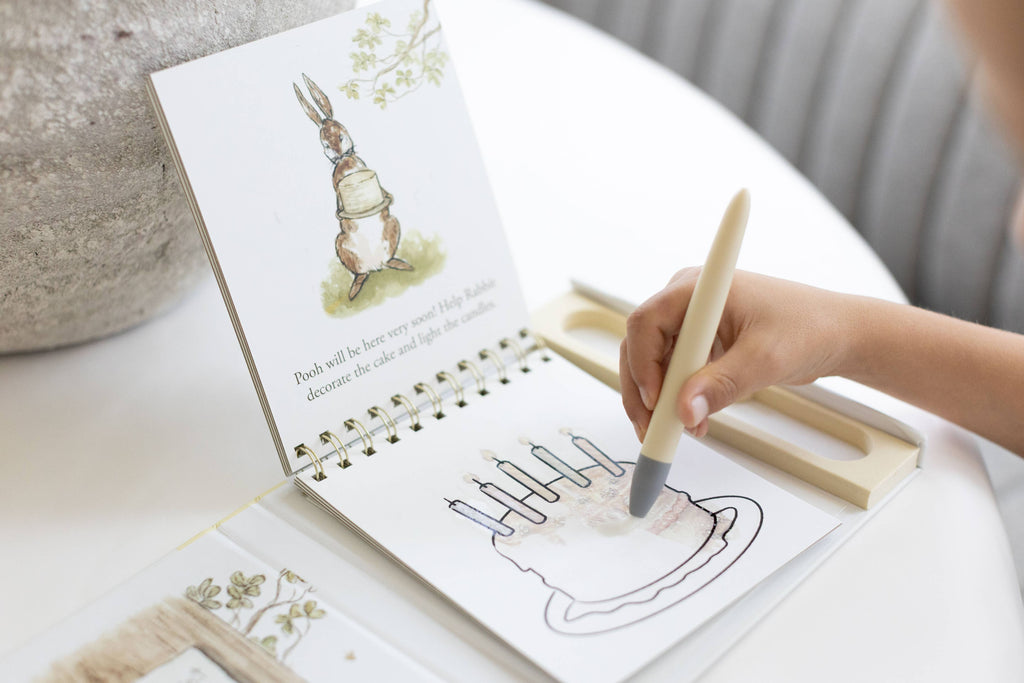 A child uses a water pen to color a cake illustration of Rabbit in a Winnie-the-Pooh: Pooh’s Birthday Surprise (Water Reveal) book.