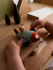 A child’s hands hold the Sabo Concept Aviator Mouse wooden toy airplane, set on a wooden surface with tree-shaped decorations—perfect for imaginative play.