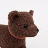 A close-up of Pull-Along Raoul, a brown, curly-textured plush bear with black eyes and a dark nose, wearing a reddish-brown collar and set against a plain white background. This adorable toy is perfect for encouraging gross motor skills in young children.