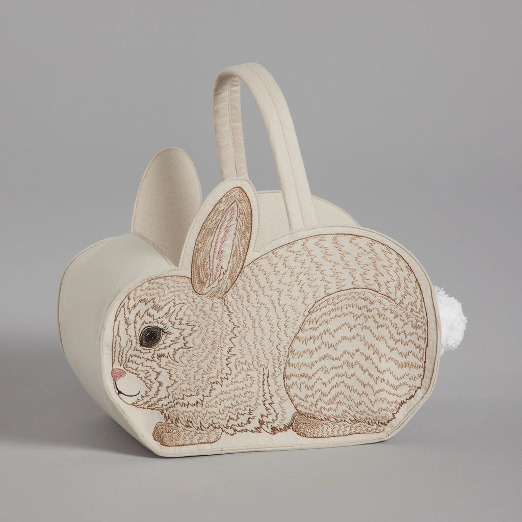 A charming Coral & Tusk Bunny Basket shaped like a beige bunny with detailed embroidery, designed with a fluffy tail and sturdy handles, on a gray background.