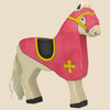 The Holztiger Tournament Horse, Red (ships in one week), is a handcrafted wood figurine with pink covering, yellow trim and cross, white mane and tail, black hooves, and a white face set against a plain background.