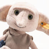The Steiff Harry Potter “Dobby” with Sock 10" plush toy features large floppy ears, green eyes, a beige tunic, a yellow Steiff tag on one ear, and is displayed against a white background.