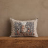 A Coral & Tusk Spooky Forest Pocket Pillow featuring embroidered bare trees, pumpkins, and a central ghostly skull face sits against a plain wall on a wooden surface.