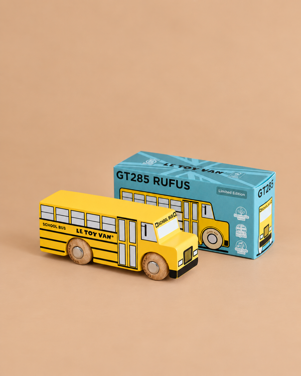 A yellow wooden school bus with black accents is displayed next to its blue and teal box labeled “No. 47 GT285 Rufus | Made in England.” Perfect for imaginative play, this retro toy features “School Bus” and “Le Toy Van” text on its side.