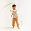 A young boy swings Sarah's Silk Robin's Egg Blue Streamer Wand attached to a stick, creating arcs in the air, dressed in a beige t-shirt and golden pants against a light background.
