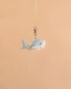 The Bukowski - Splash Shark Bag Charm, a small plush shark keychain perfect for cuddling, hangs from a beige ribbon against a plain peach background.