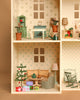 The Maileg Fully Furnished Holiday Dollhouse Set includes floral wallpaper, dollhouse furniture, a mini Christmas tree with ornaments, wrapped gifts, sofa, armchair, rocking chair, lamp, and coffee table with cups and pastries.