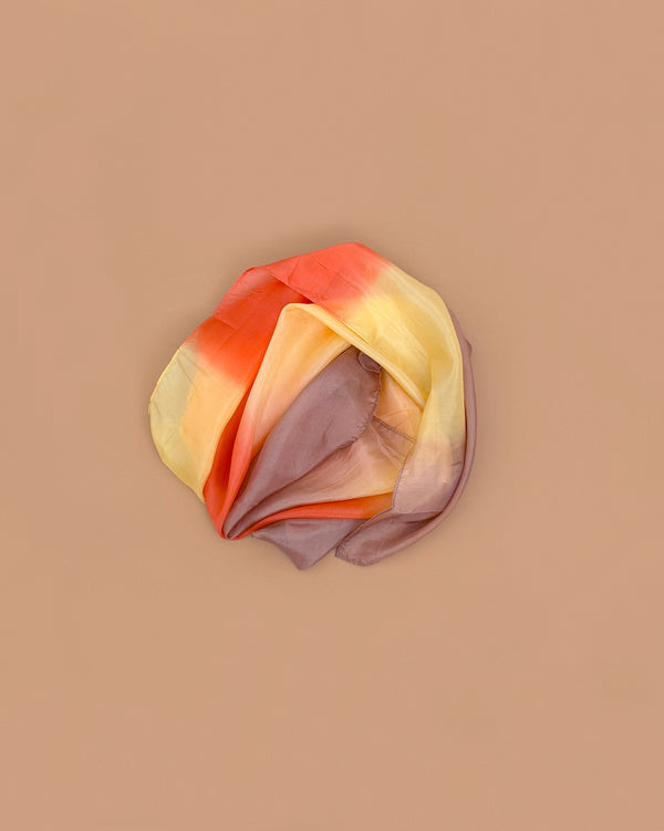 Sarah's Silks Earth Playsilk - Desert, a pure silk scarf with gradient shades from yellow and orange to light purple, is loosely folded on a light brown background—ideal for open-ended play and imaginative moments.