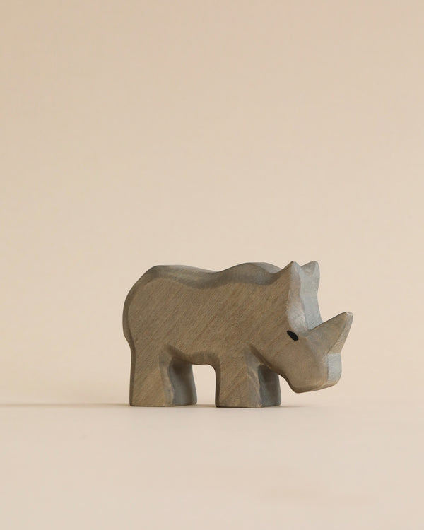 A simple Handmade Holzwald Baby Rhino on a light beige background. The figurine, crafted as a high-quality wooden toy, is stylized with smooth lines and minimal detail, highlighting the artistry.