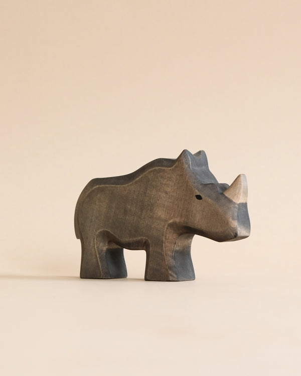 A high-quality Handmade Holzwald Rhino sculpture positioned against a plain, light beige background, showcasing detailed carvings and smooth, dark finish.