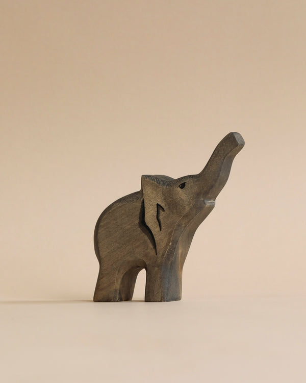 A high-quality Handmade Holzwald Baby Elephant figurine stands against a plain beige background. The elephant is carved with visible wood grain and stylized features, including an uplifted trunk.
