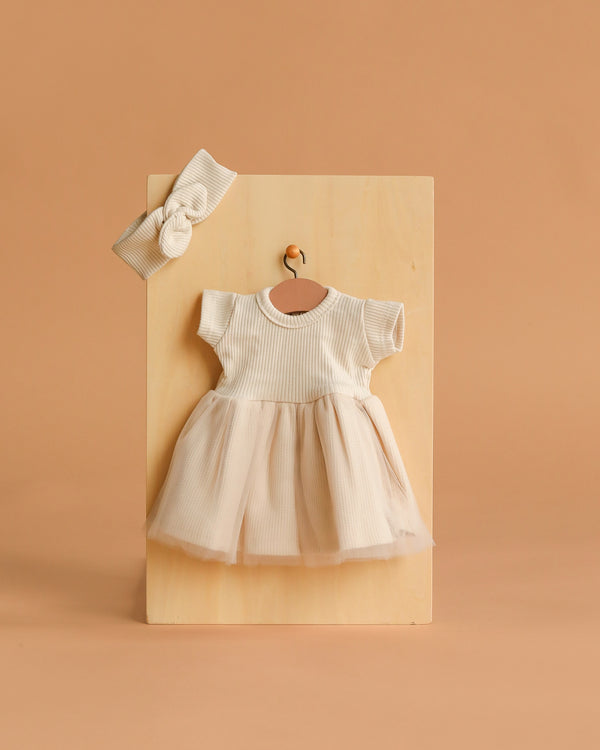 The Minikane 11" Doll Clothing | Rosana Short-Sleeved Tutu and Headband - Linen features a cream linen dress with short sleeves and a tulle skirt, plus a ribbed headband, perfect for your Minikane doll—shown on a wooden board against a beige background.