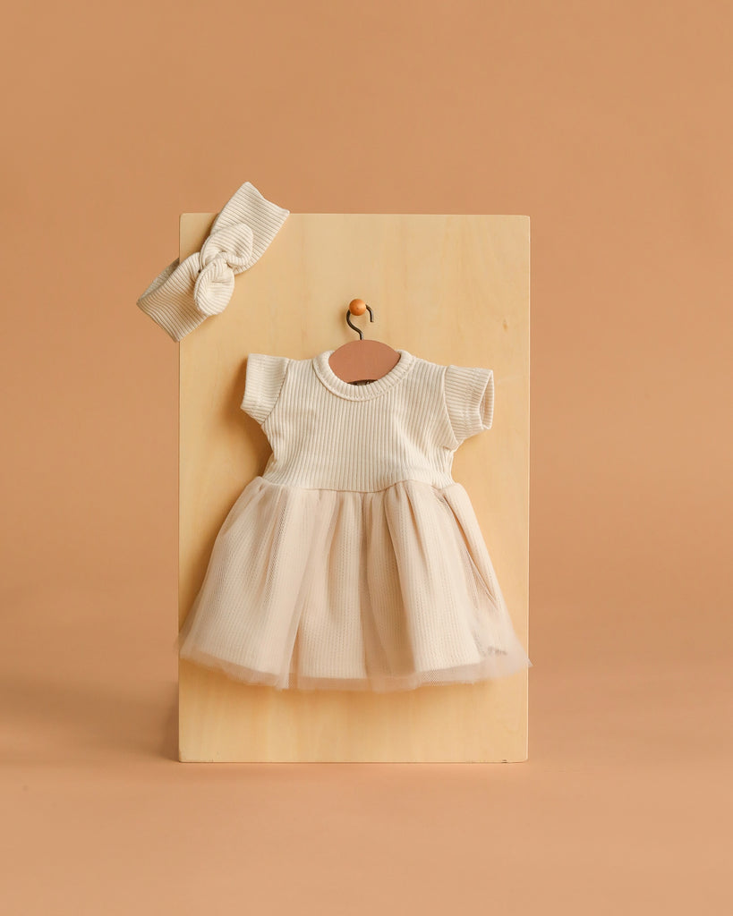 The Minikane 11" Doll Clothing | Rosana Short-Sleeved Tutu and Headband - Linen features a cream linen dress with short sleeves and a tulle skirt, plus a ribbed headband, perfect for your Minikane doll—shown on a wooden board against a beige background.