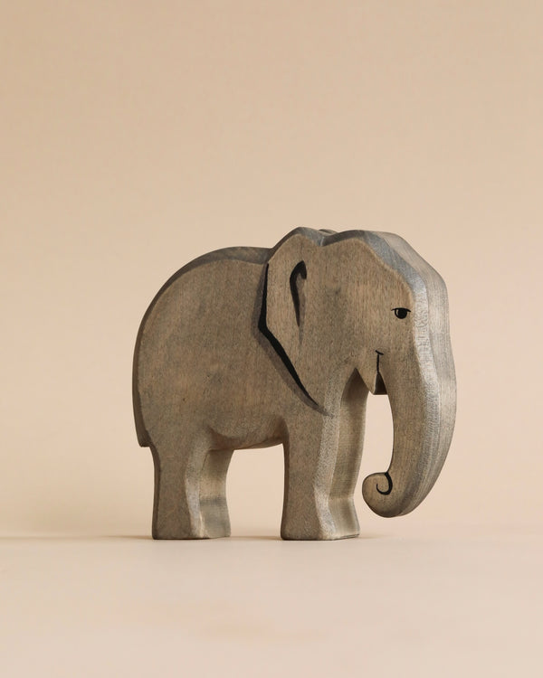 A Handmade Holzwald Elephant figurine stands against a plain beige background, featuring visible wood grain and carved details such as eyes and ears. It's an example of sustainable toys crafted from environmentally-friendly materials.