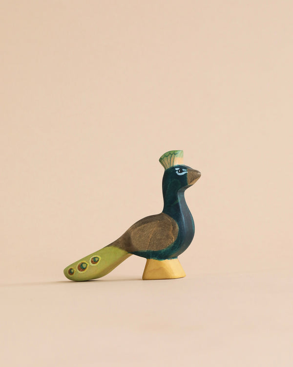 A colorful wooden Handmade Holzwald Peacock figurine with a stylized design, featuring shades of green, blue, and brown, displayed against a soft beige background. This piece is crafted from sustainable wooden toys materials.