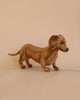 A realistic model of a brown Dachshund Stuffed Animal with a smooth coat and blue eyes standing against a plain beige background, crafted as an artisan handmade plush animal.