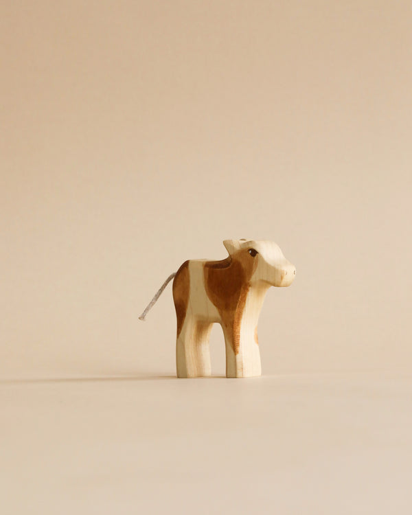 A Handmade Holzwald Calf, with a light and dark brown pattern, standing against a plain beige background. The calf has a simplistic design, and its gentle expression makes it perfect among sustainable toys