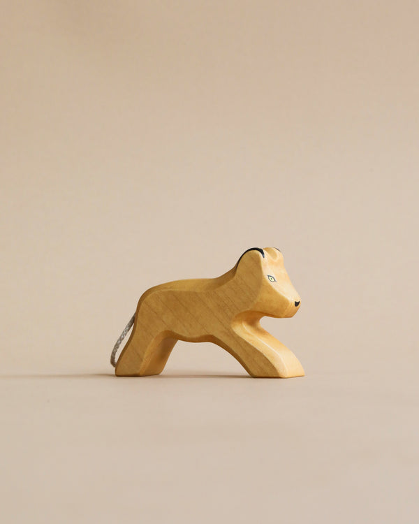A Handmade Holzwald Lion Cub figurine on a plain beige background, showing a simple and smooth carved design with visible grain texture.