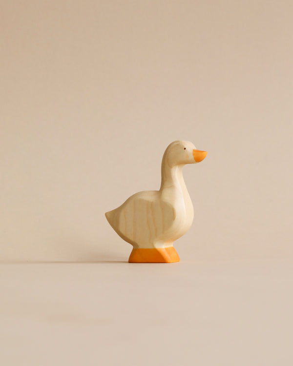 A Handmade Holzwald Goose carving with a smoothly polished surface, standing on a plain beige background. The goose is depicted in mid-stride with its head held high.