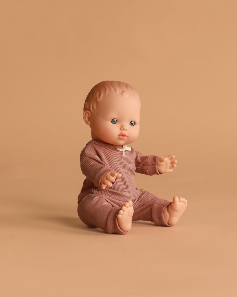 The Minikane Vintage Baby Doll (13") - Rosalie with Clothing features blue eyes, light skin, and a ribbed brown outfit. This anatomically correct doll sits on a beige surface, seamlessly blending style and authenticity.