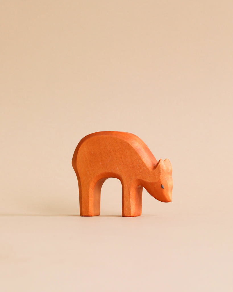 A handmade Holzwald eating deer figurine on a plain beige background. The figurine is simplistic, with a smooth finish and minimalistic details emphasizing its curved back and elongated snout. This piece
